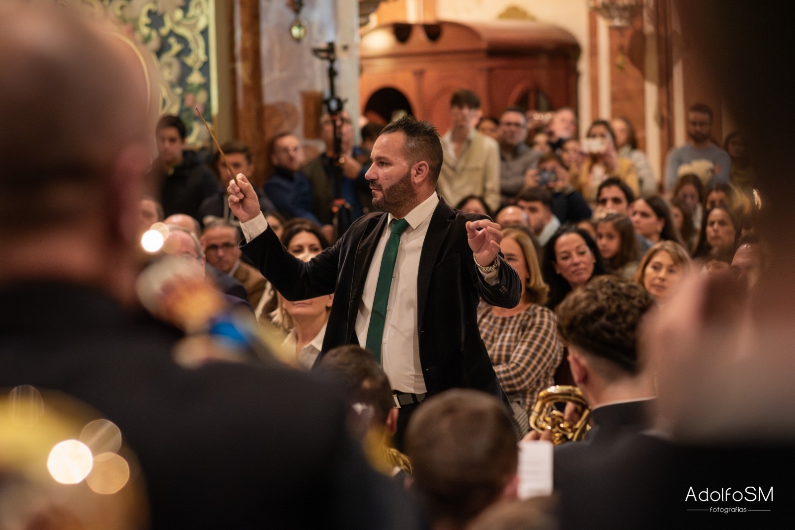 Concierto con el público al fondo y Manu Guerrero dirigiendo con corbata verde