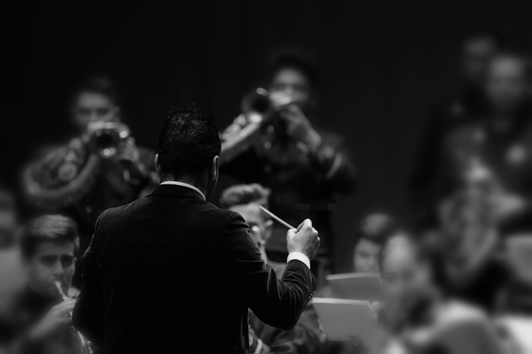 Manu Guerrero de espaldas dirigiendo con batuta a la sección de metales